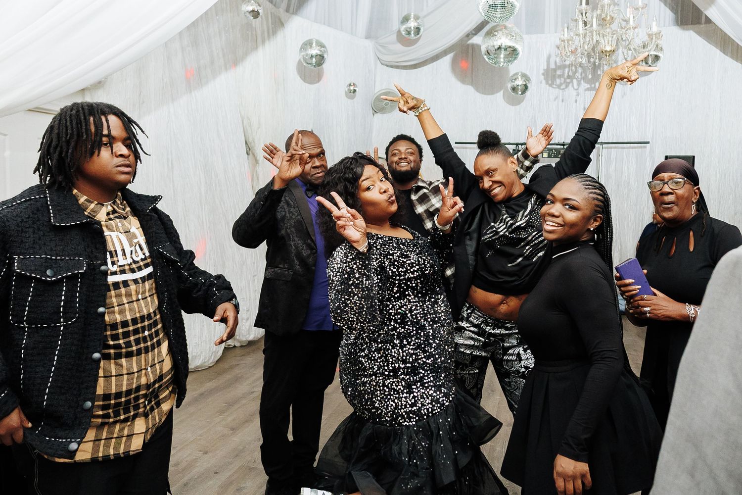 Group of joyful people dancing and celebrating at a festive party under disco balls in a white tent.