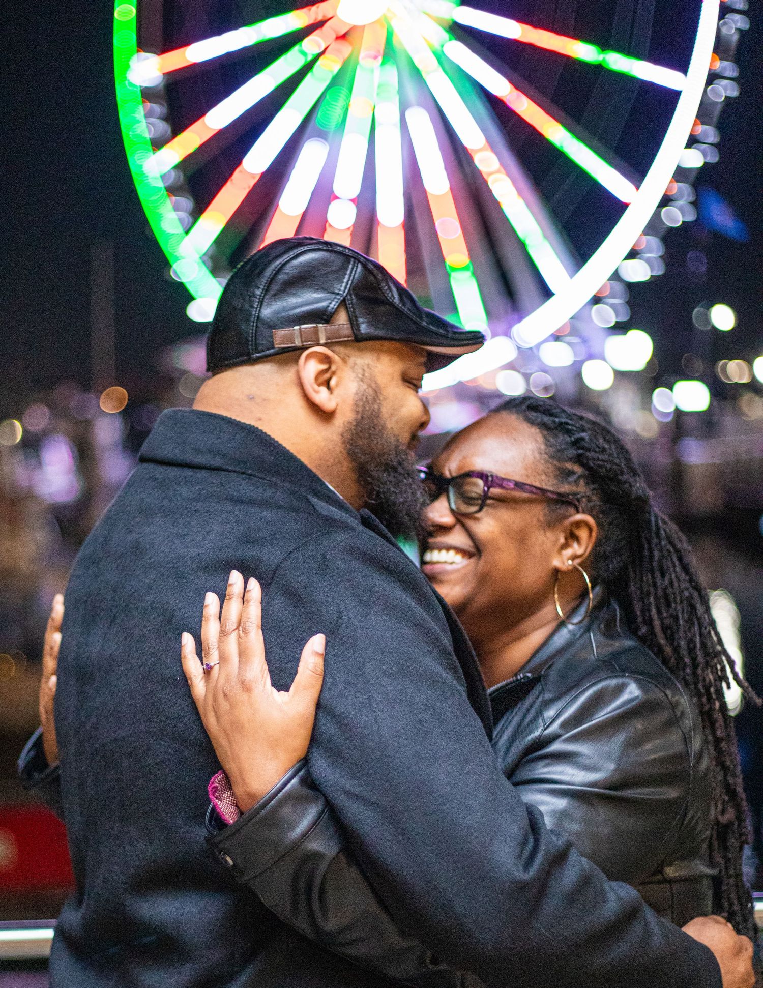 A tender moment shared against the backdrop of a colorfully illuminated Ferris wheel at night.