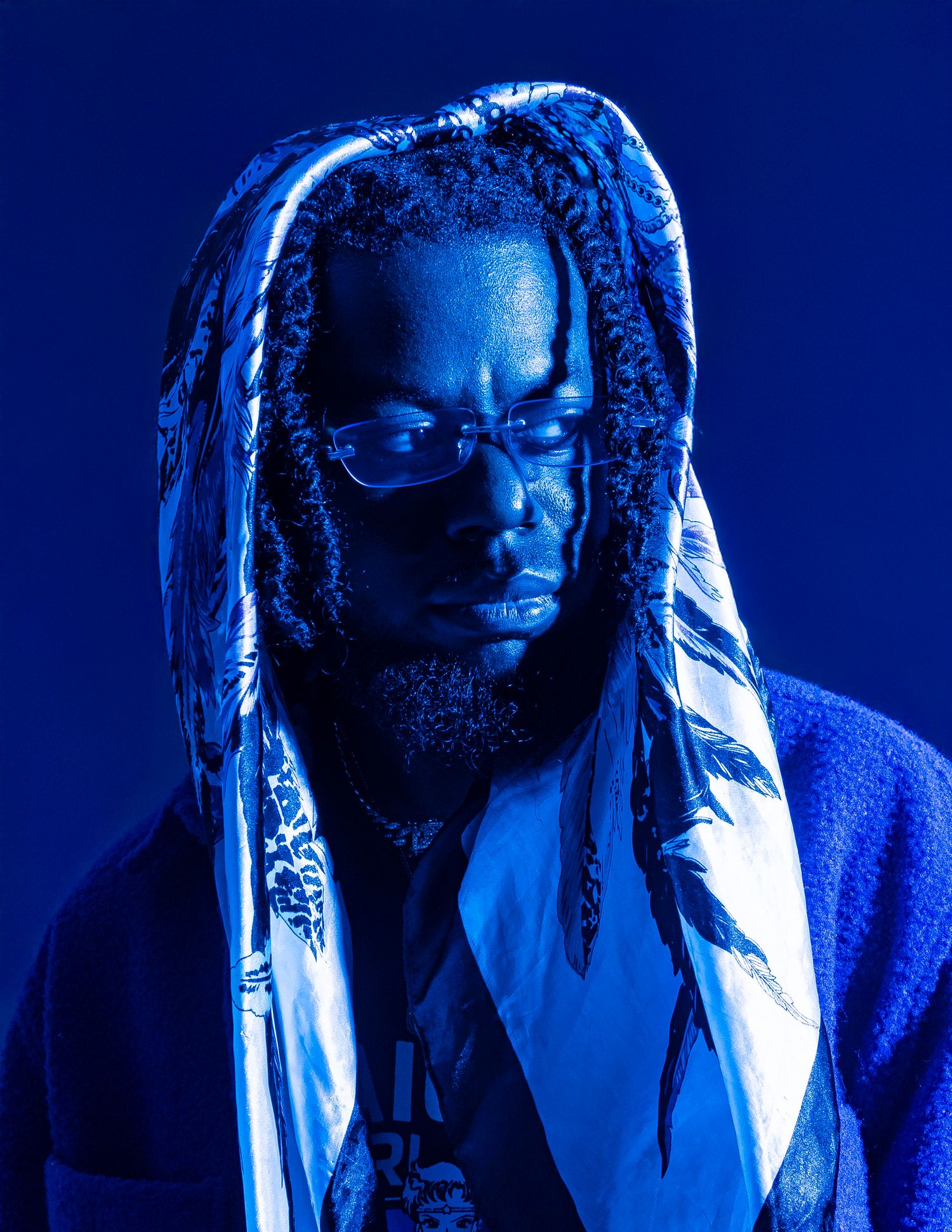 Person with long braided dreadlocks illuminated by dramatic blue lighting in an artistic portrait photo.