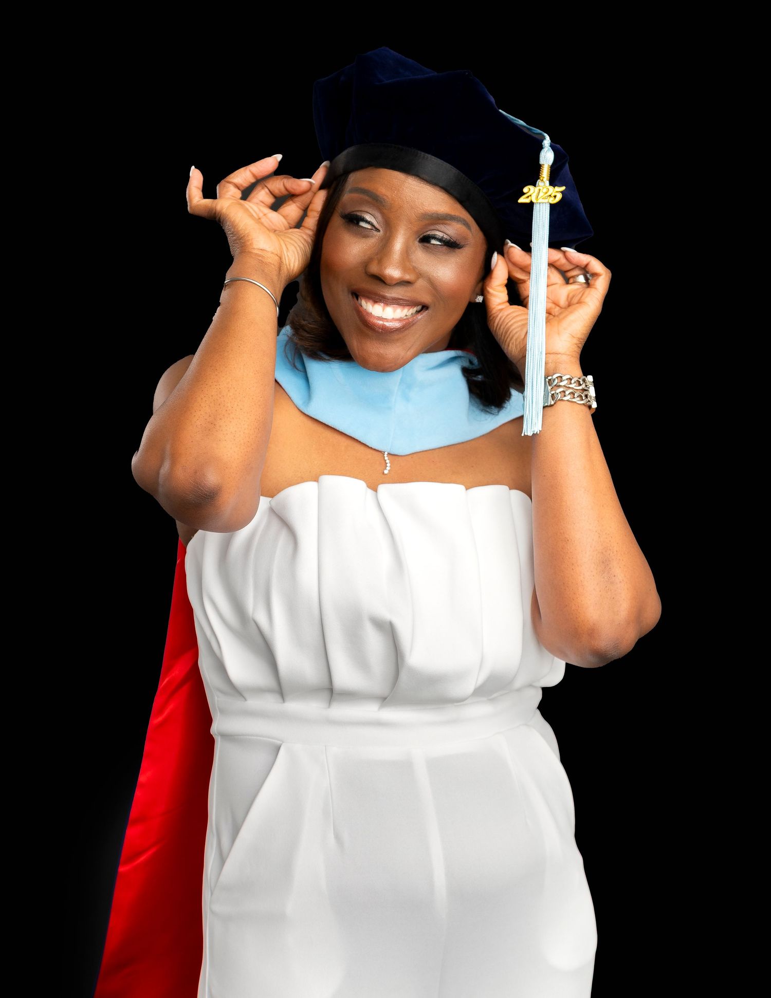 Smiling graduate woman in white dress wearing navy doctoral cap and light blue hood against black background.