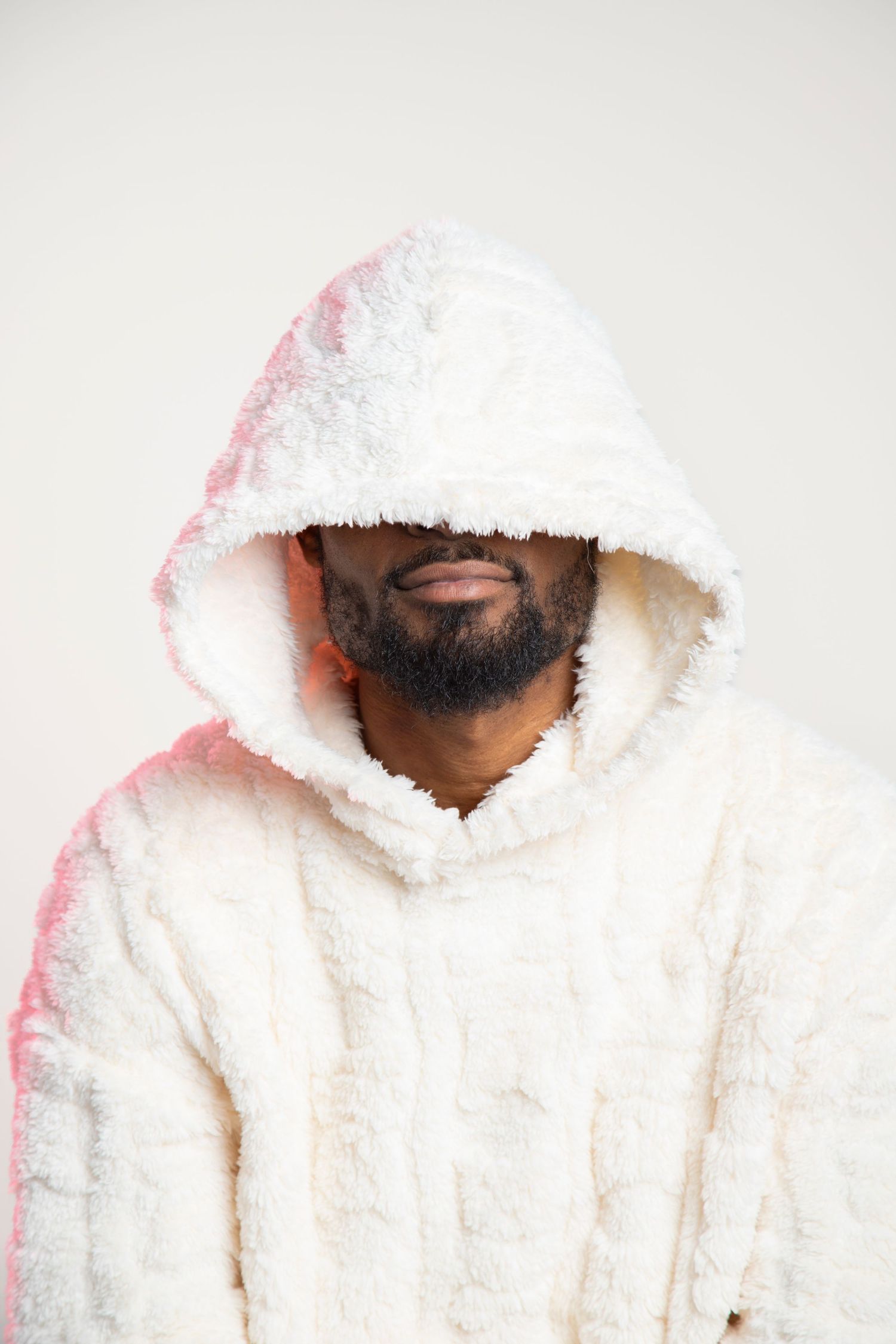 Man with beard wearing a cozy white fluffy hooded sweatshirt against a light background.