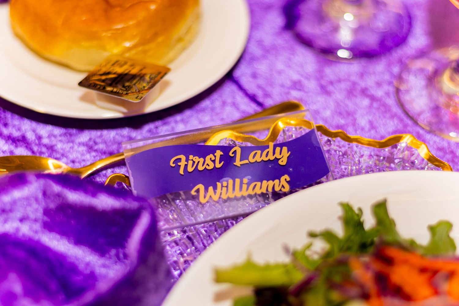 Purple and gold table setting with a name card reading First Lady Williams at an elegant formal dinner event.