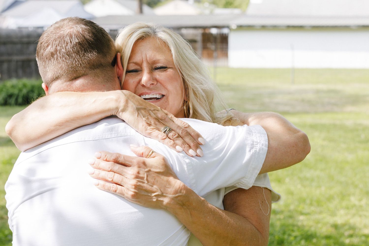 People embracing outdoors in white attire during a special occasion.