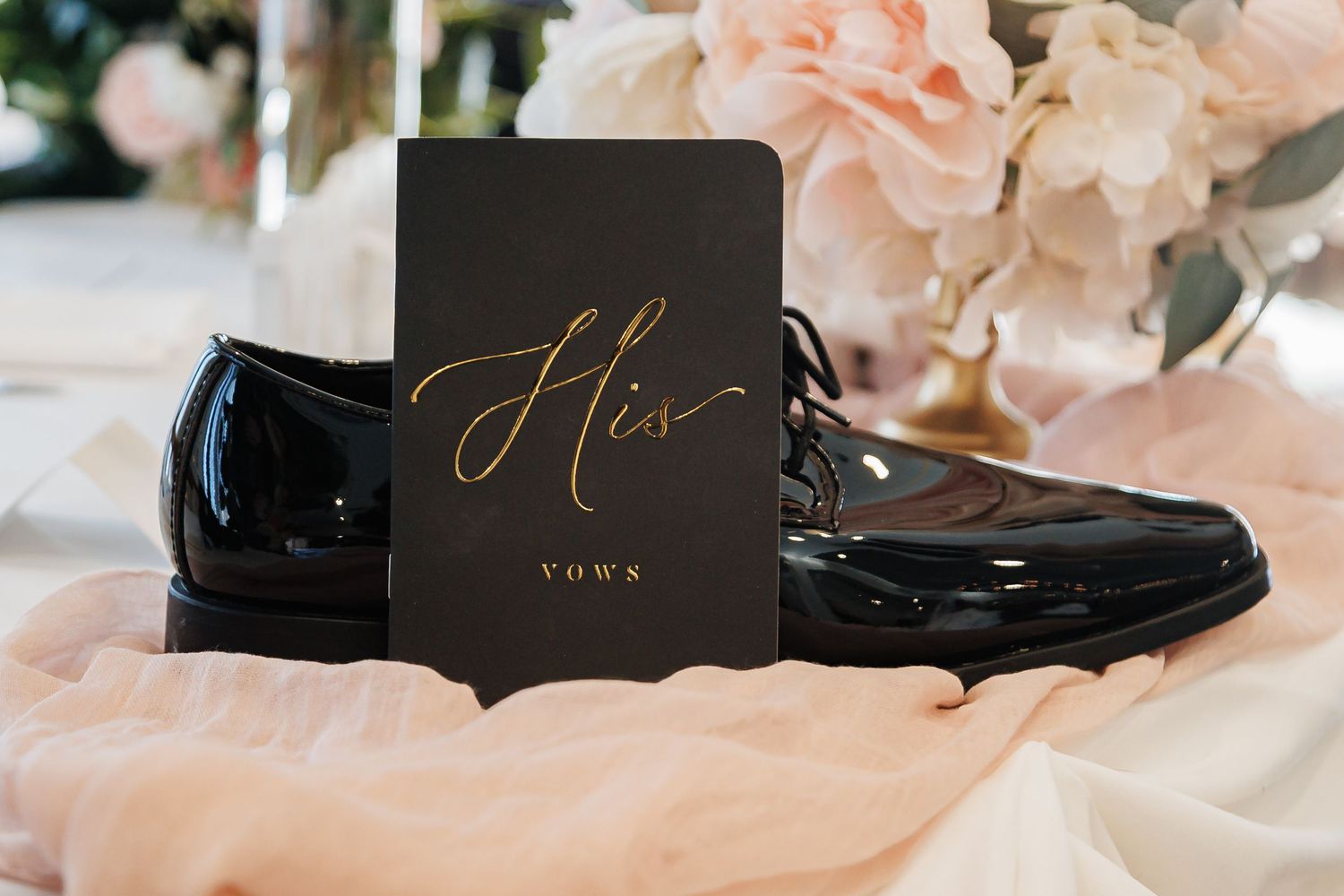 Wedding details including blush pink floral arrangements and black and gold stationery on silk fabric.