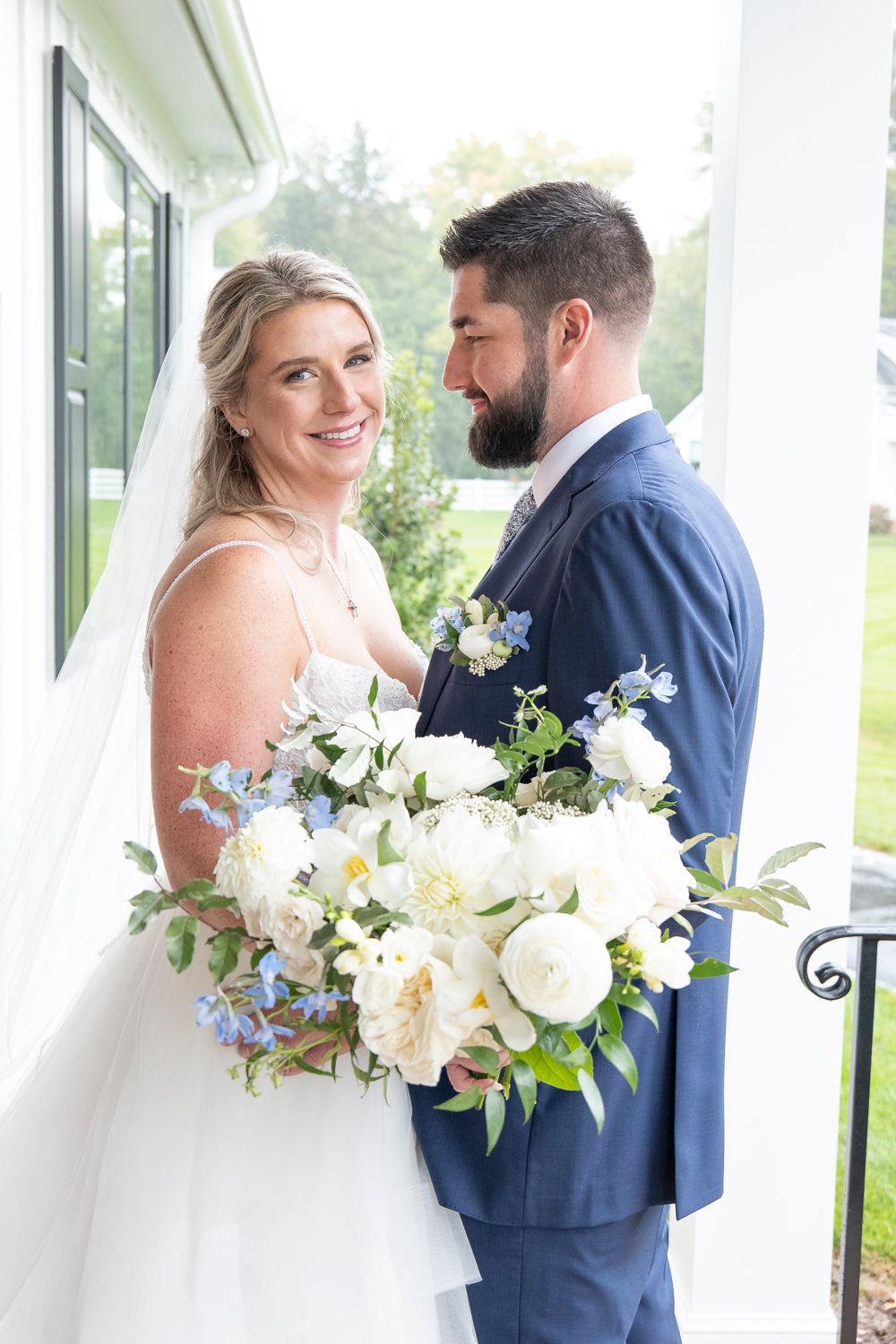 Bride and groom share tender moments in white colonnade with beautiful bouquet.
