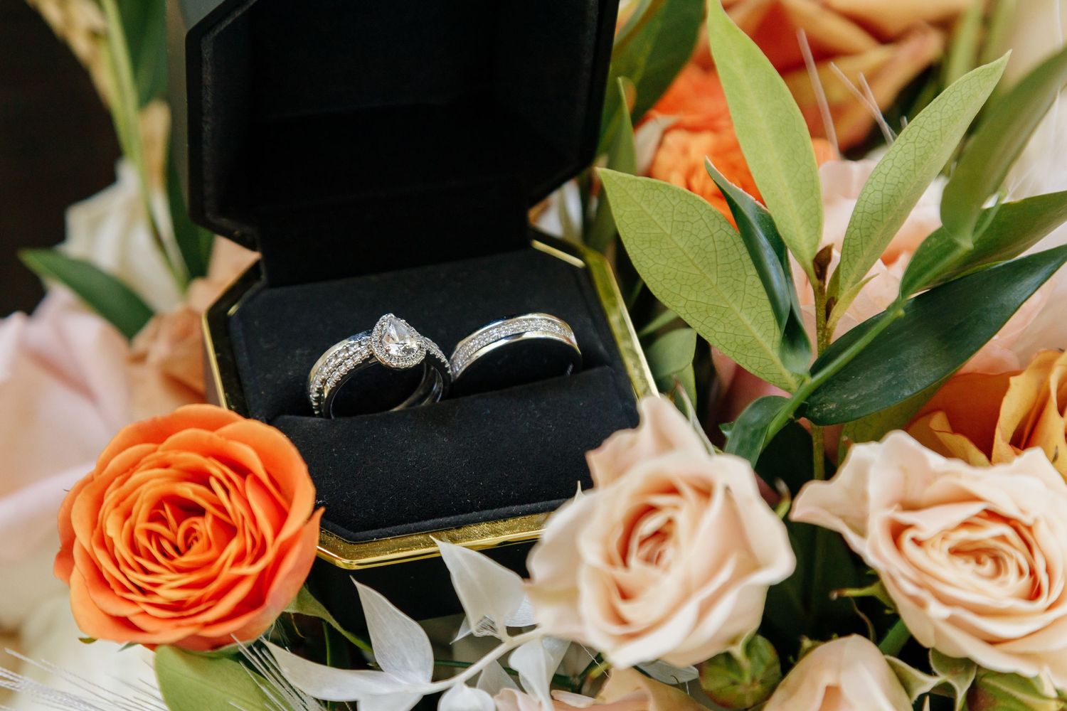 Elegant floral arrangement with orange roses and peach colored flowers against a dark background.