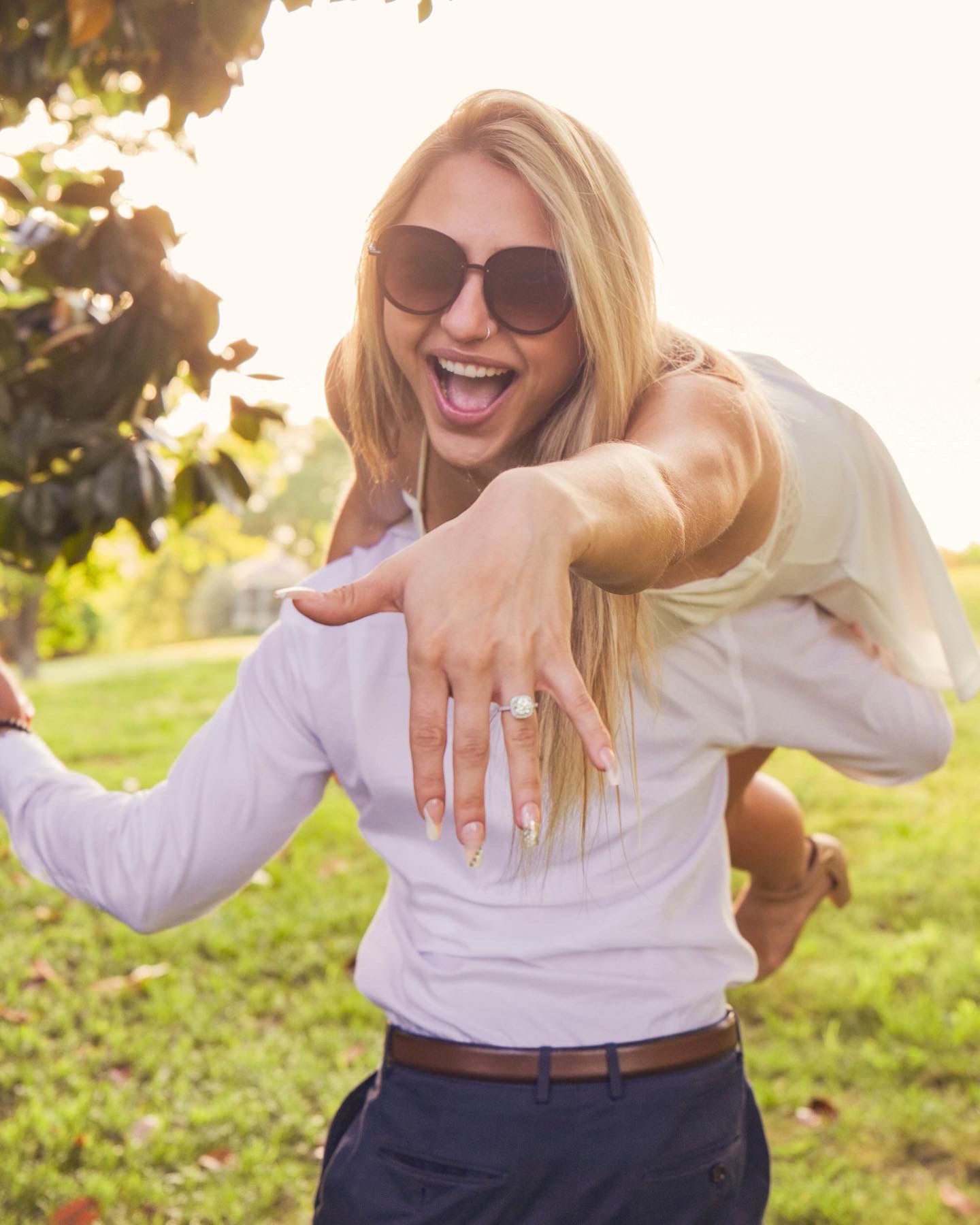 Person in white top and dark pants showing excitement outdoors in natural lighting.