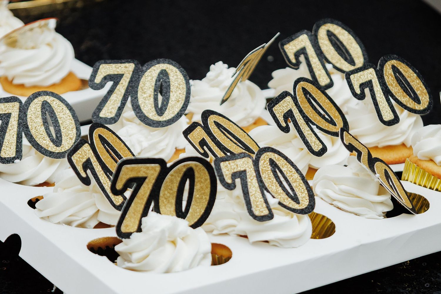 Cupcakes with white frosting topped with gold and black glittery number 70 decorations for a birthday celebration.