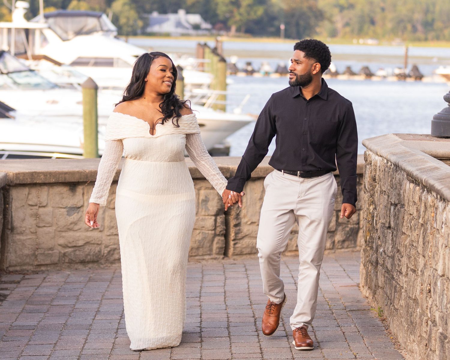 A couple enjoying a romantic moment along a stone wall overlooking a scenic waterfront view.