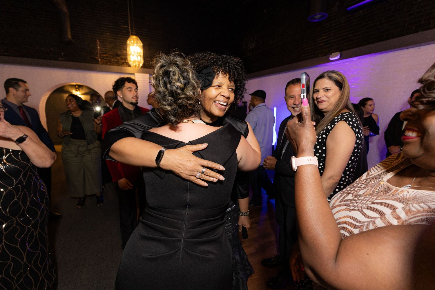 Woman in black dress dancing joyfully at a lively indoor party with guests in the background.