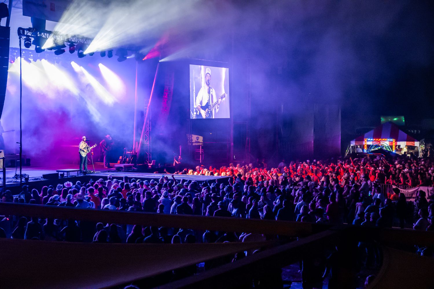 Large concert crowd watching performer on stage with dramatic purple lighting and smoke effects.