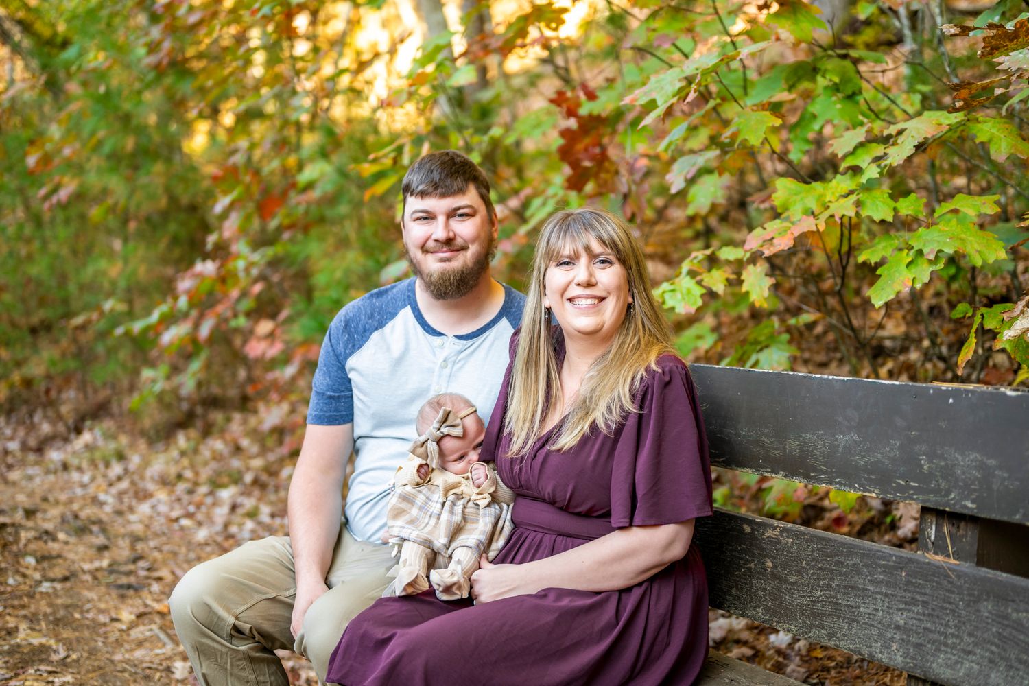Outdoor family photoshoot in wooded area with fall foliage and warm sunset lighting.