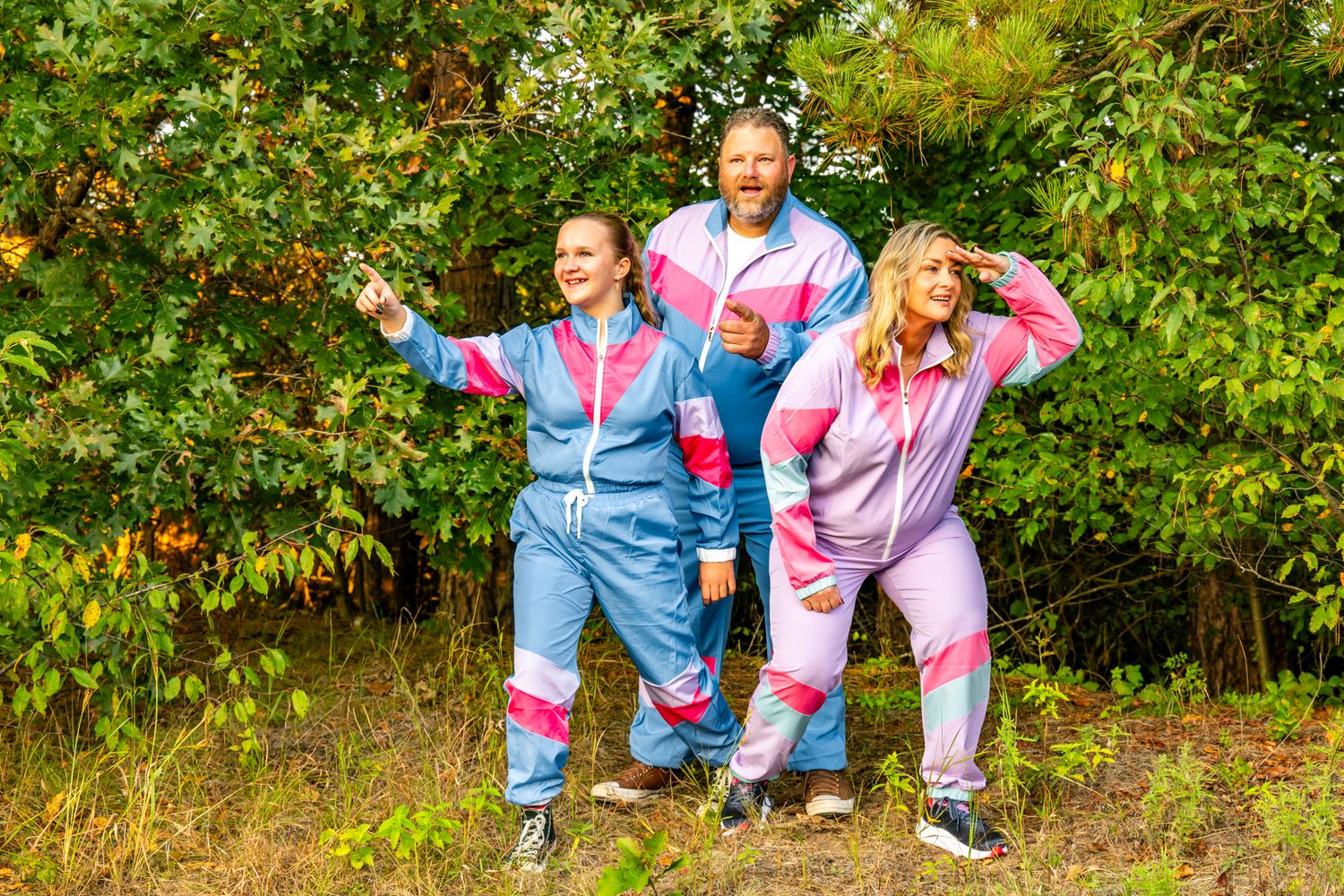 Three people in matching pastel tracksuits striking fun poses among fruit trees.