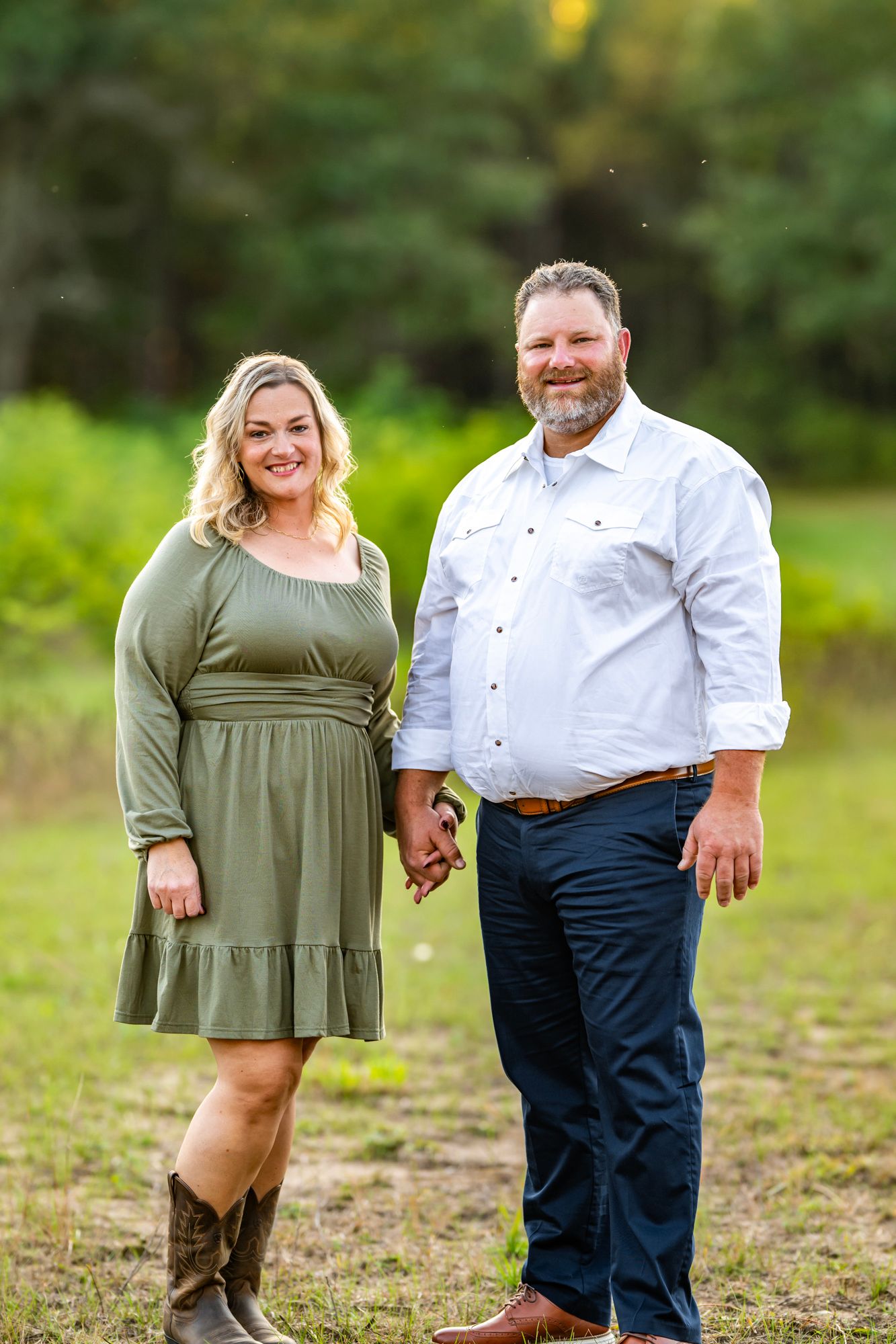 Couple in casual attire poses together on grassy field during golden hour photo session.