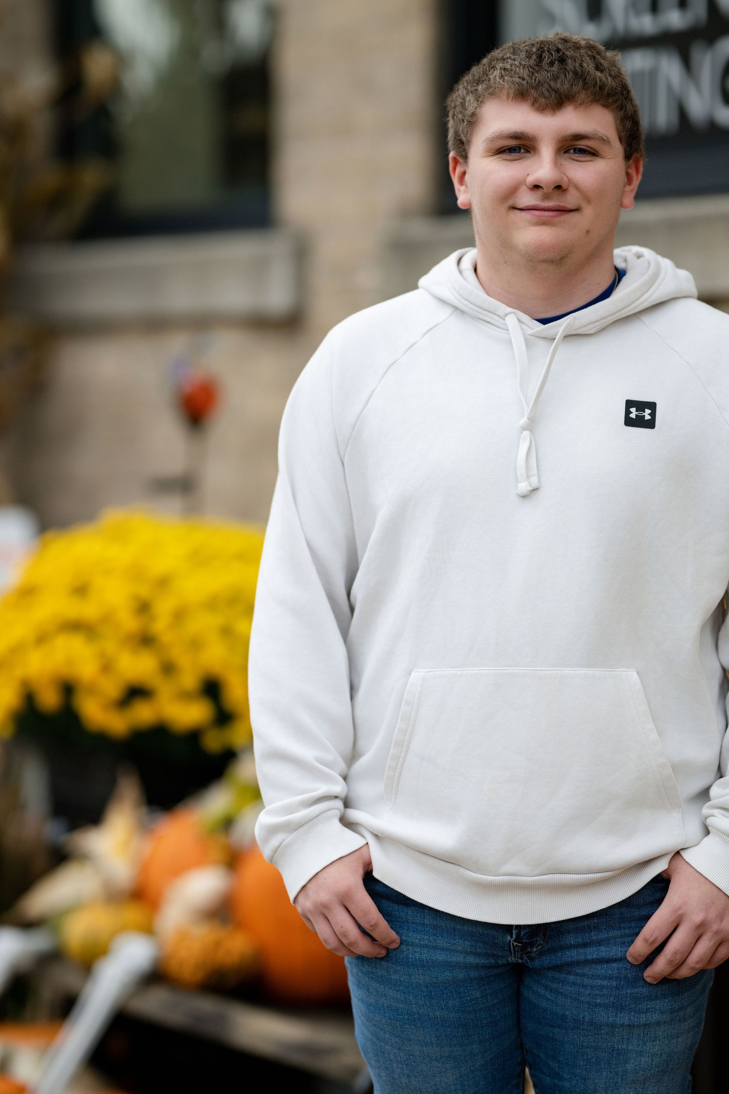 Casual portrait in white hoodie with yellow mums and pumpkins in background.