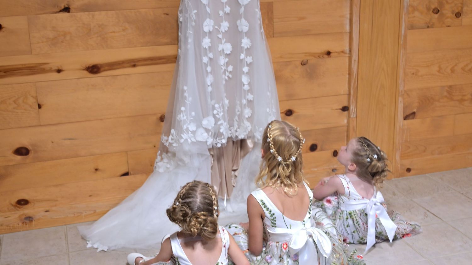 Wedding dress detail shot with bridesmaids sitting on wooden floor.