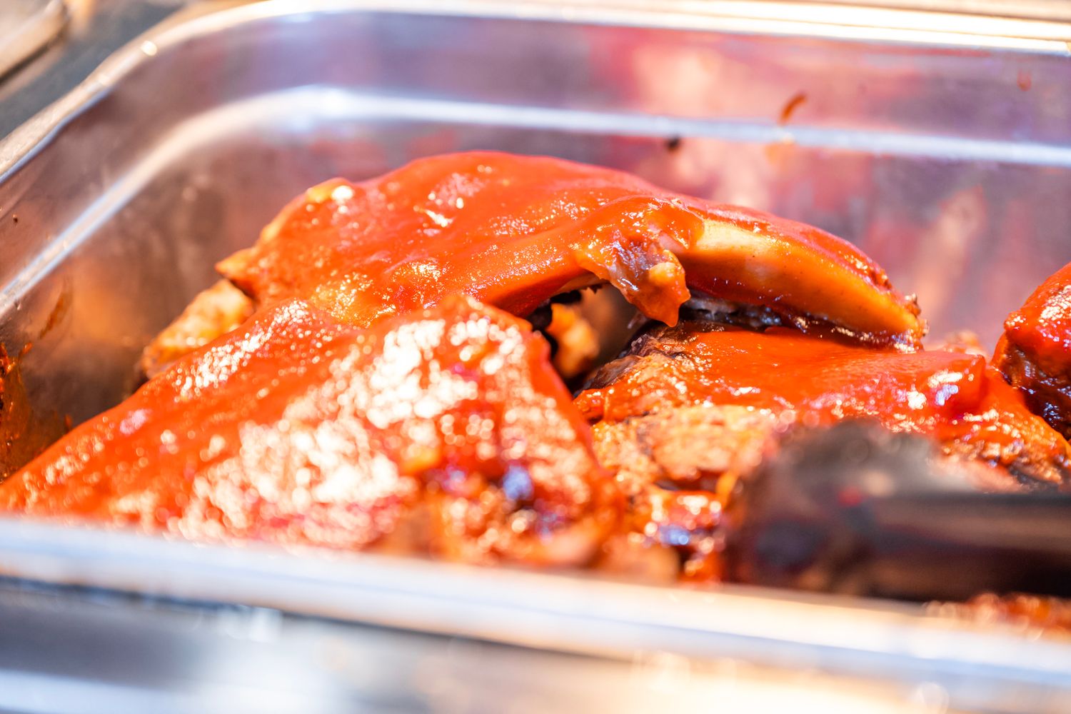 Close up of glazed chicken wings in a metal serving tray with bright red sauce.