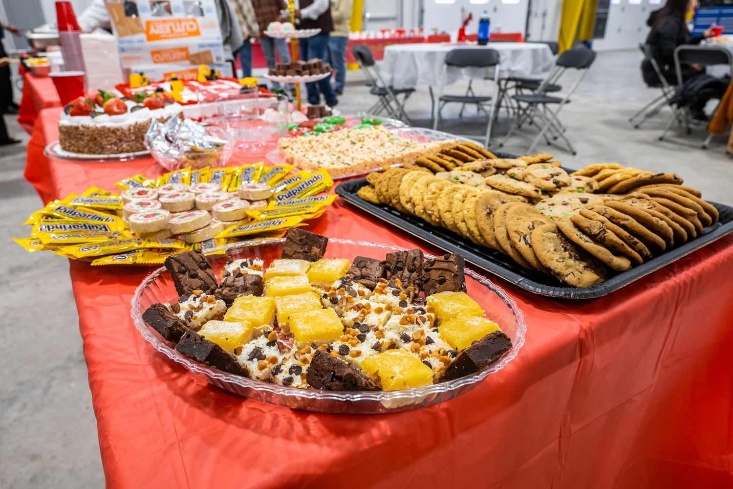 Dessert table with pastries and baked goods displayed on red tablecloths at a community event.