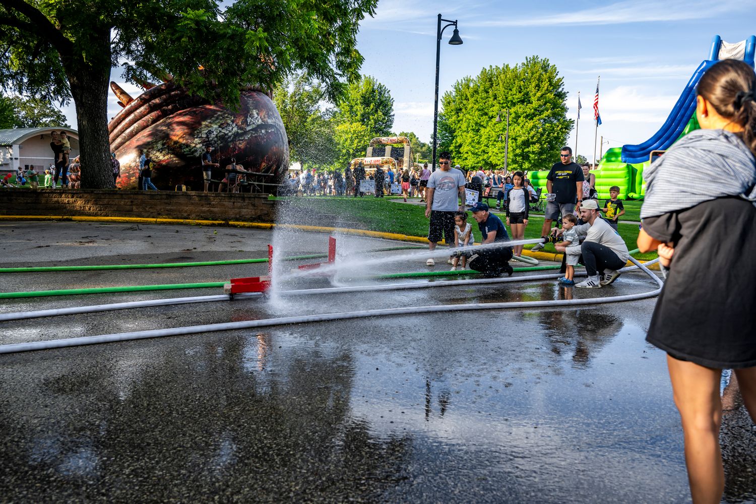 Wet pavement reflects people and tents at an outdoor community event on a rainy day.