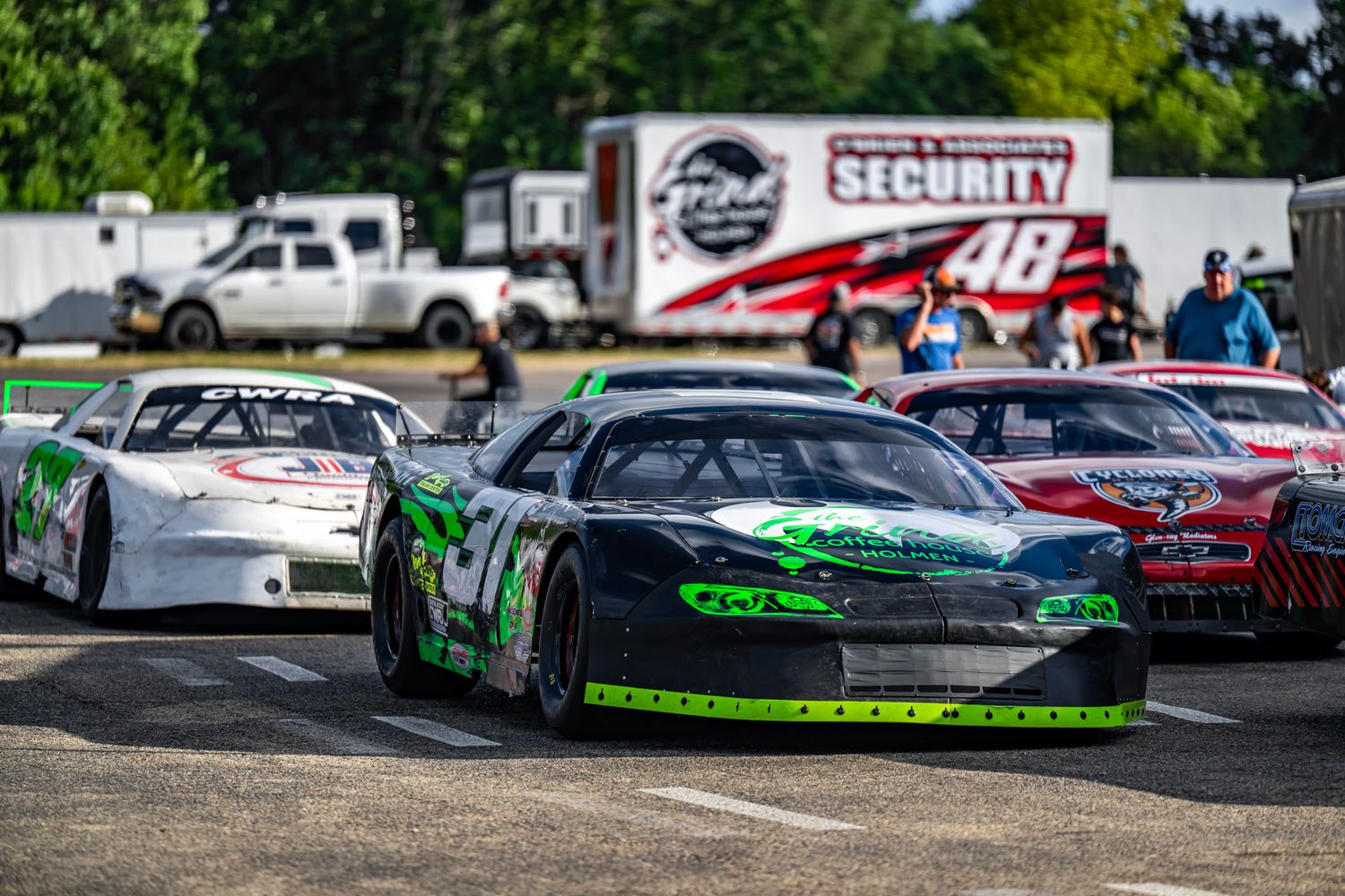 Multiple stock cars lined up on a racing track during a competition event.
