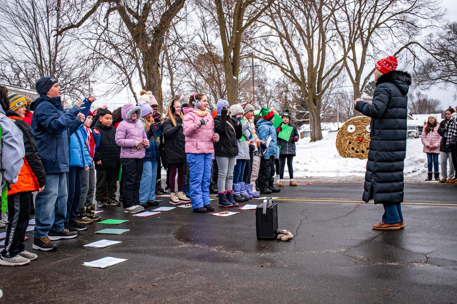 Crowd gathered outdoors in winter for holiday event with snow-covered trees in background.