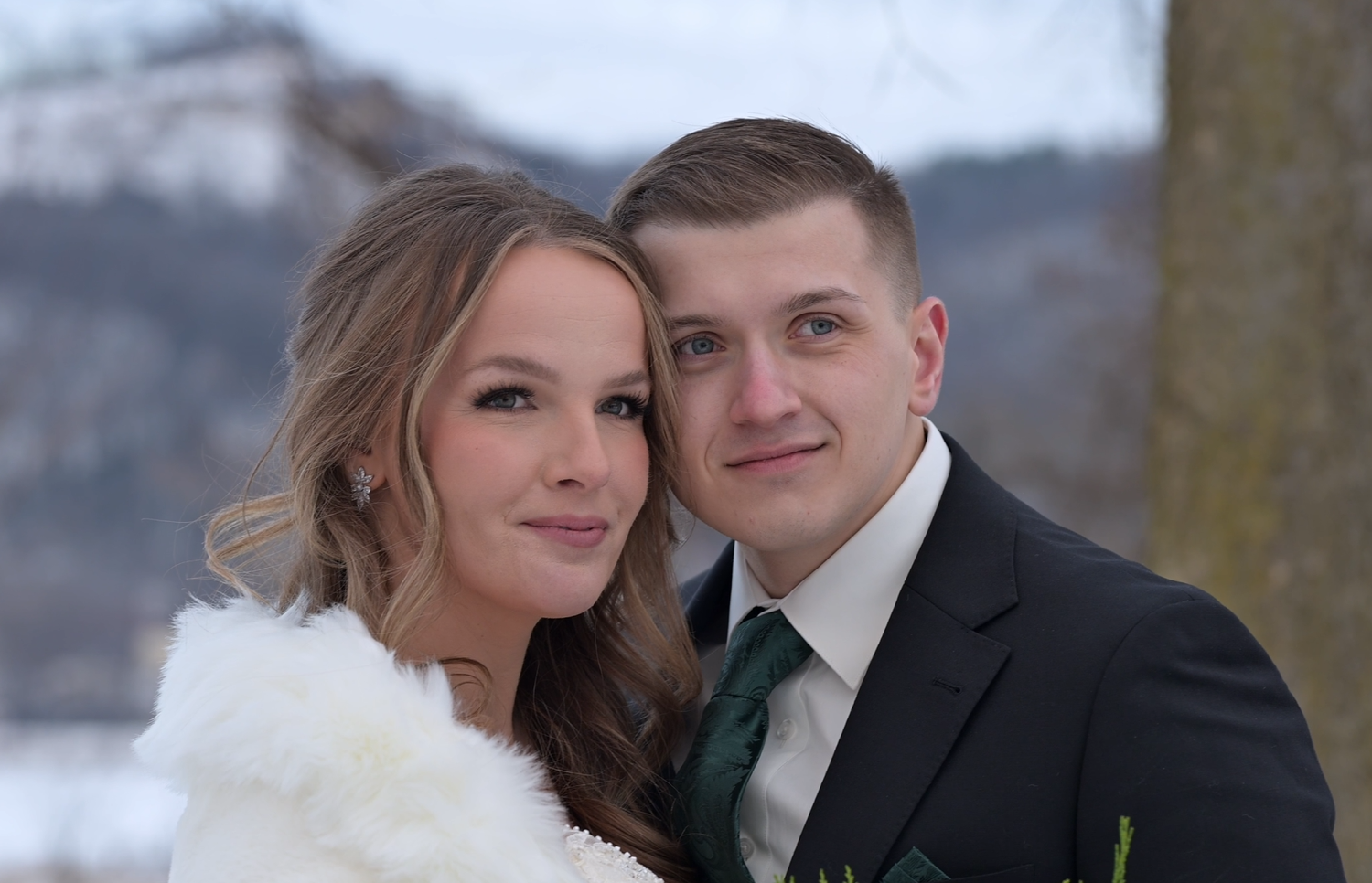 Romantic winter wedding portrait with snow-covered landscape in background.