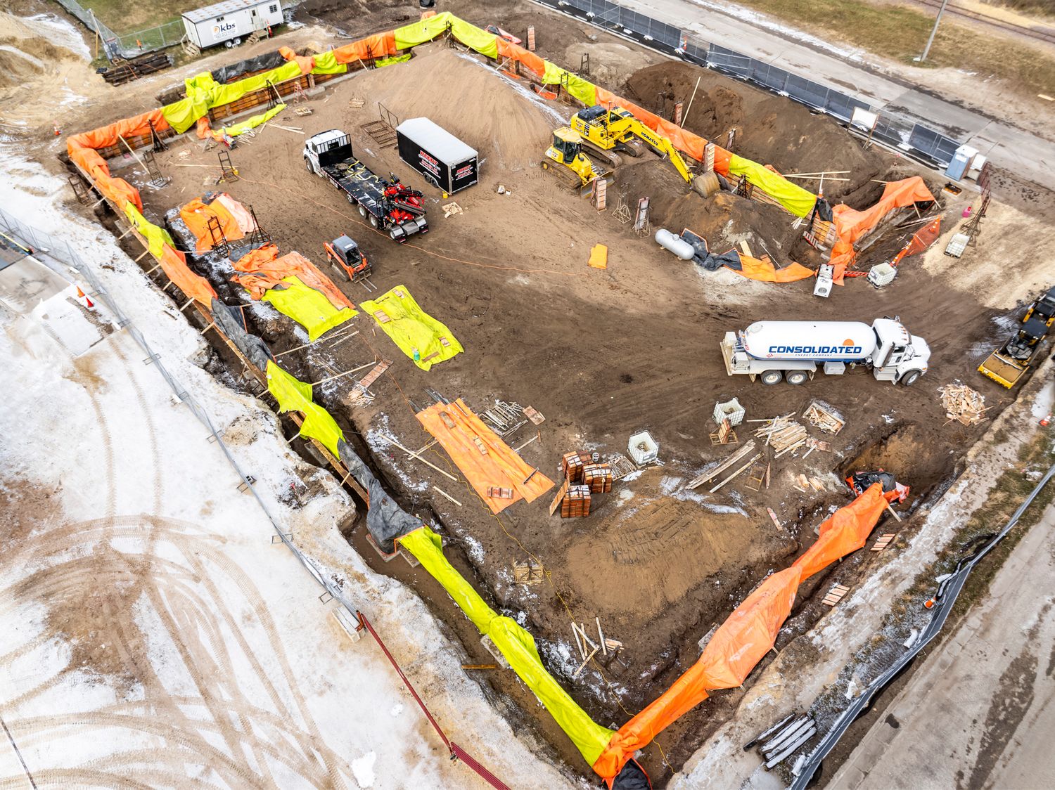 Aerial view of construction site with yellow and orange safety barriers forming a perimeter.