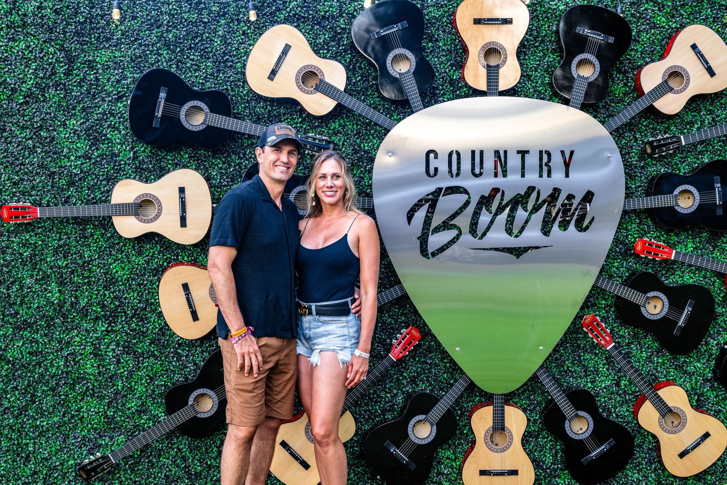 Decorative display of acoustic guitars arranged against a green hedge wall with country music theme.