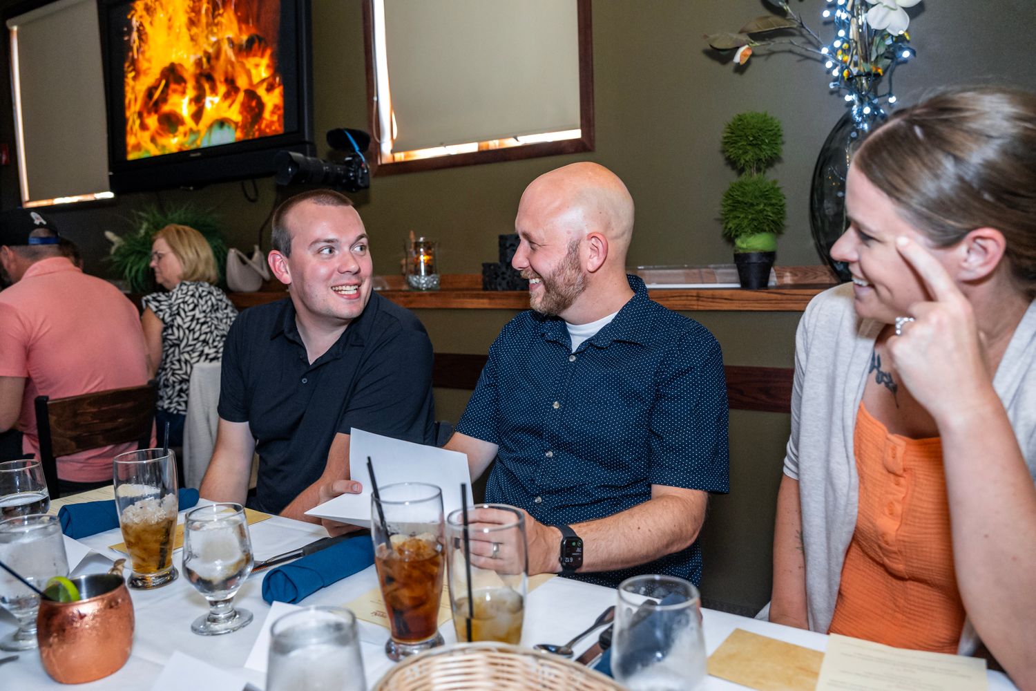 Friends enjoying drinks and conversation at a restaurant table with a fireplace in the background.