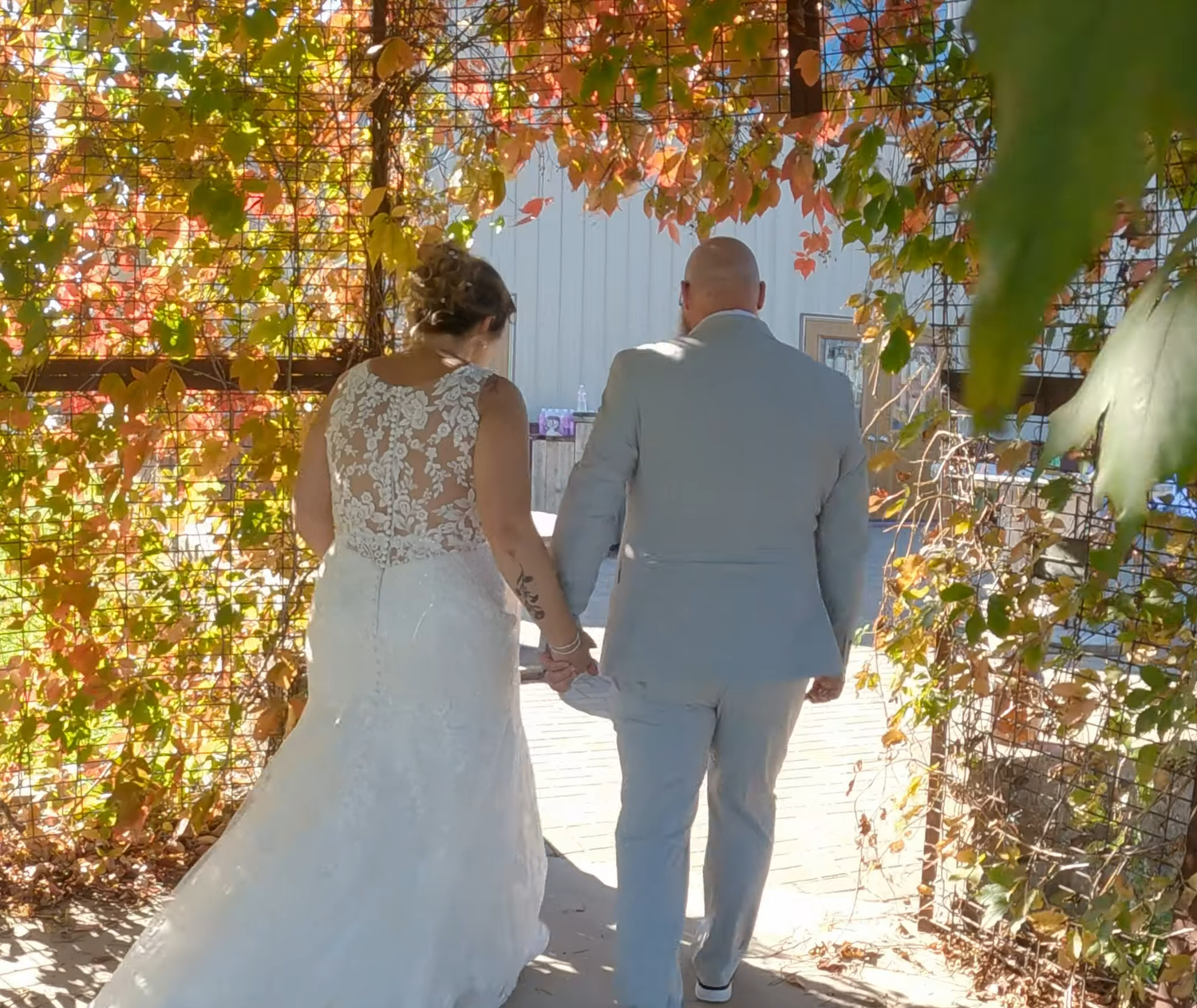 Romantic autumn wedding photo of couple walking under colorful fall foliage.