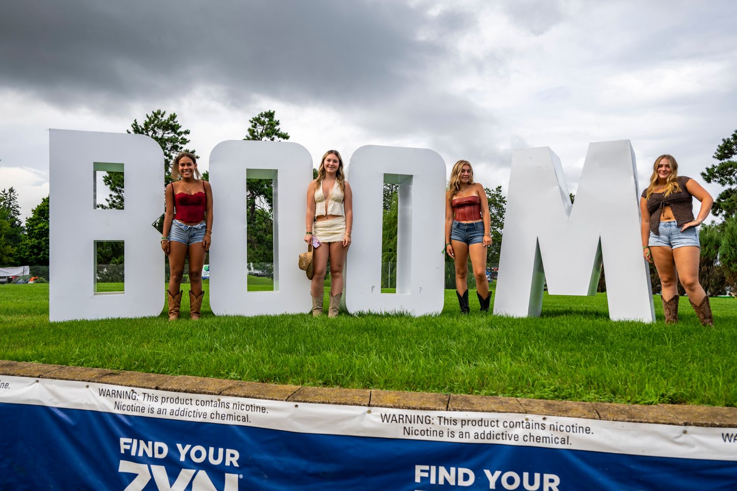 Festival goers stand in front of large white BOOM letters at a country music festival.
