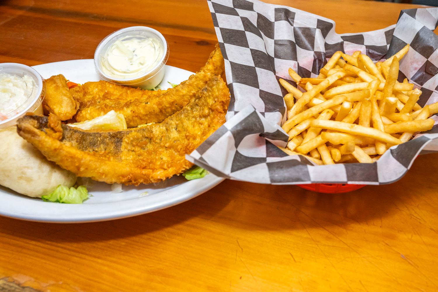 Beer battered fish and chips served with tartar sauce and french fries in a checkered basket.
