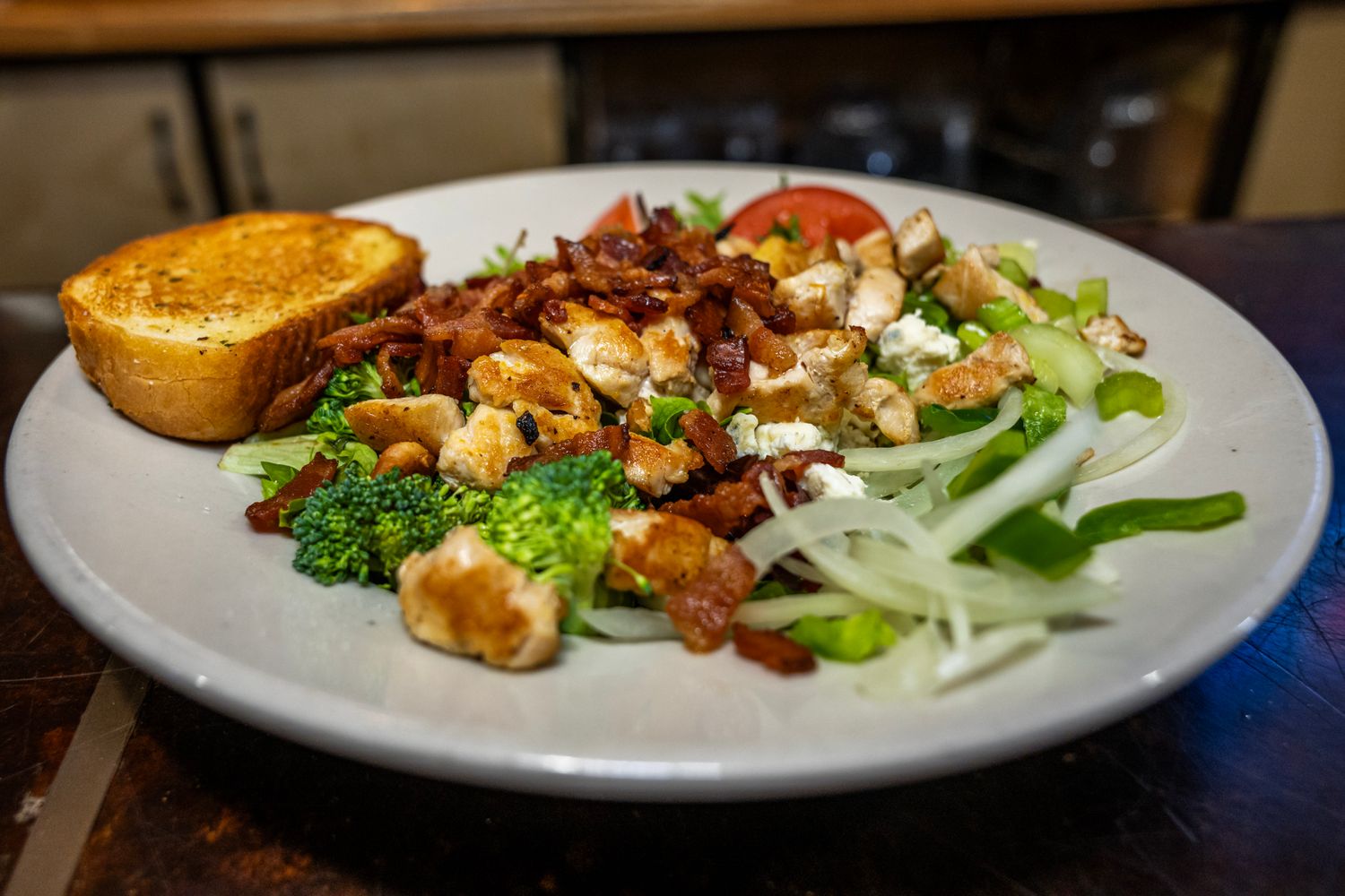 Colorful salad with grilled meat, fresh vegetables and toasted bread served on a white plate.