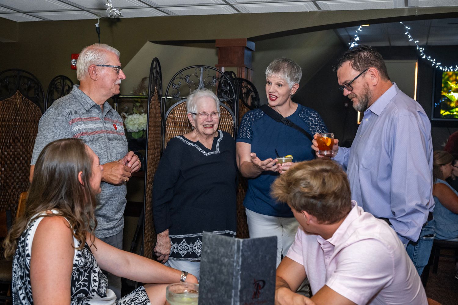A group of people gathered around a table sharing conversation and laughter at an indoor event.