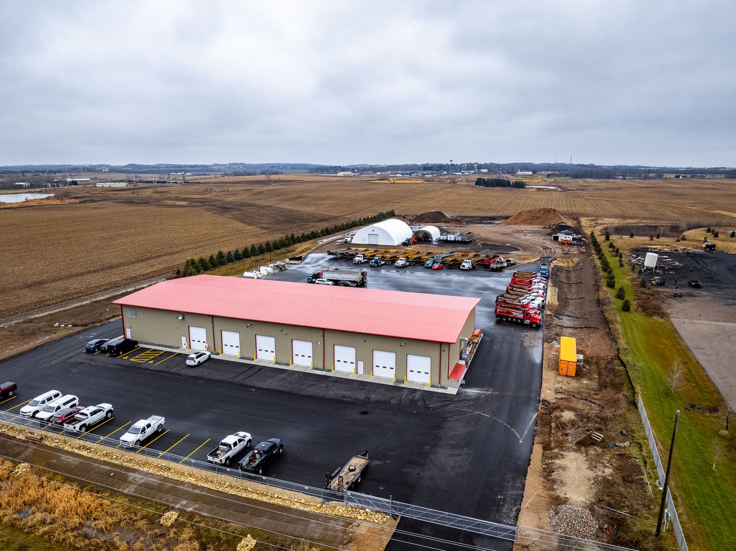Aerial view of a large industrial building with red roof and parking lot in a rural area.