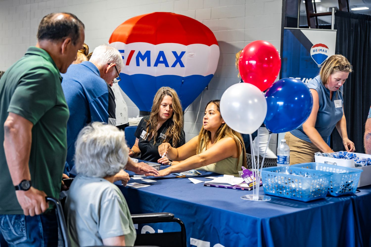 Event setup with RE/MAX branded decorations including balloons and a promotional table.