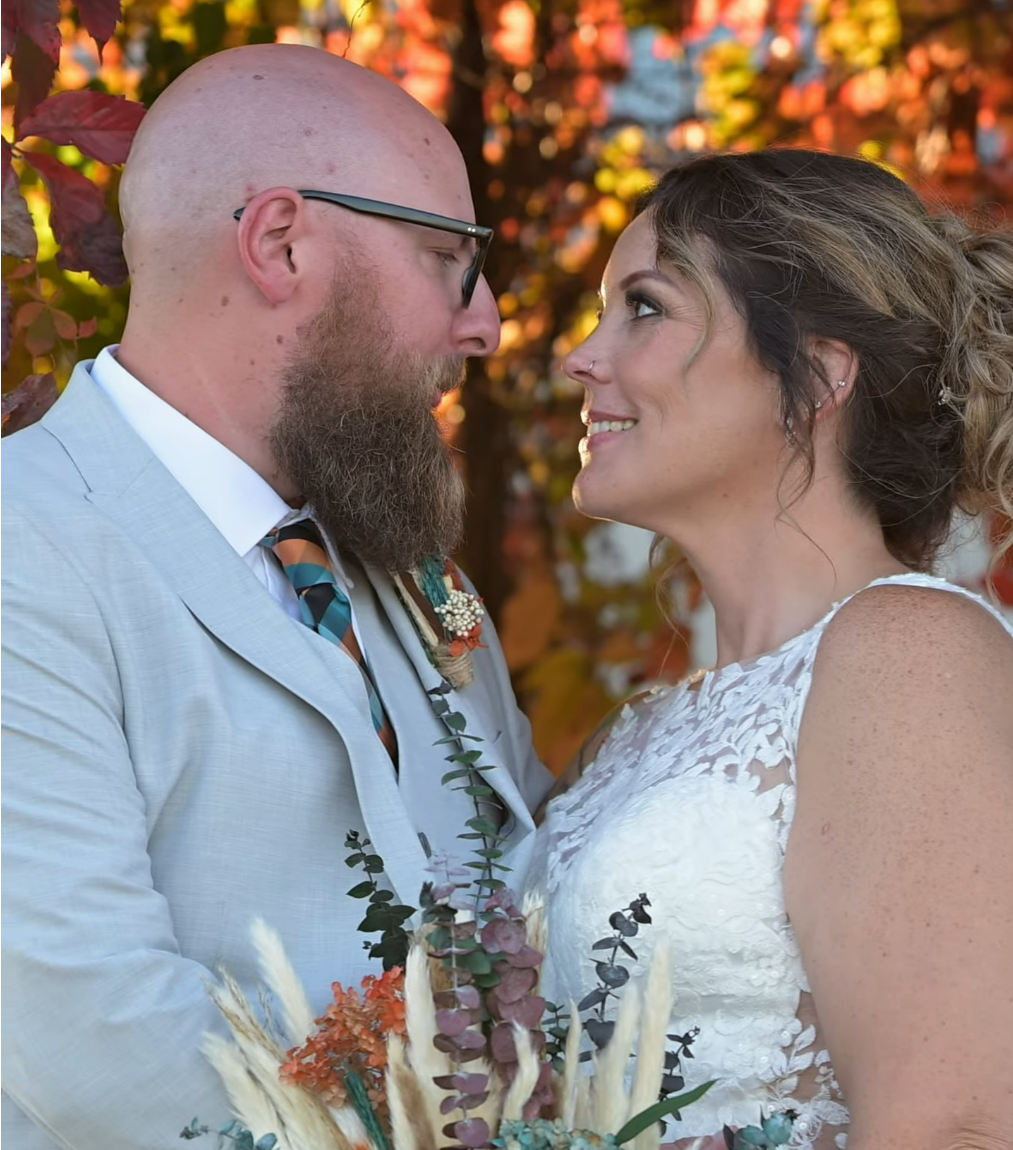 A couple shares joyful moments during their autumn wedding with colorful foliage in background.