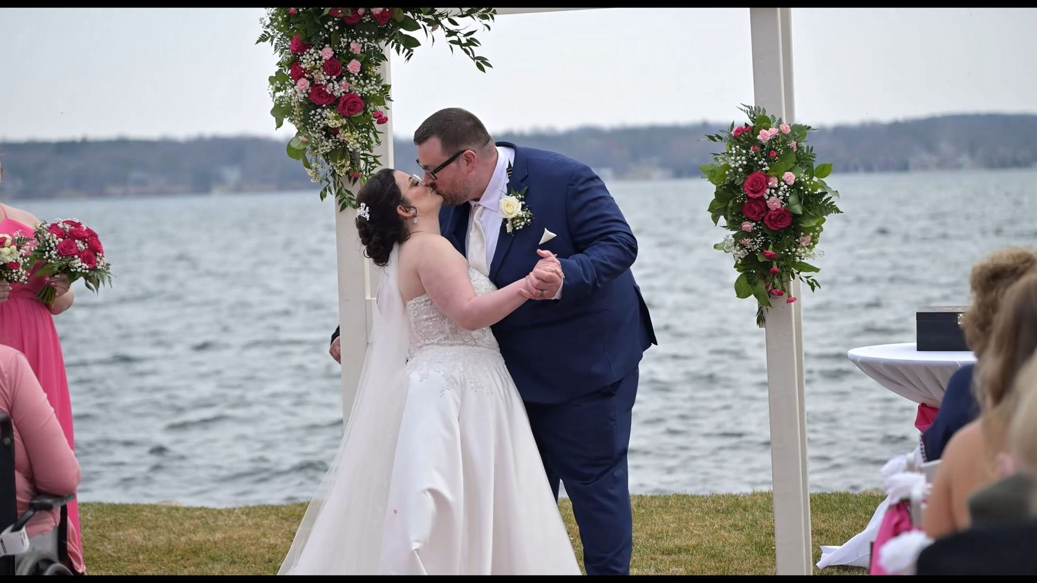 Outdoor wedding ceremony setup with floral arch and waterfront view.