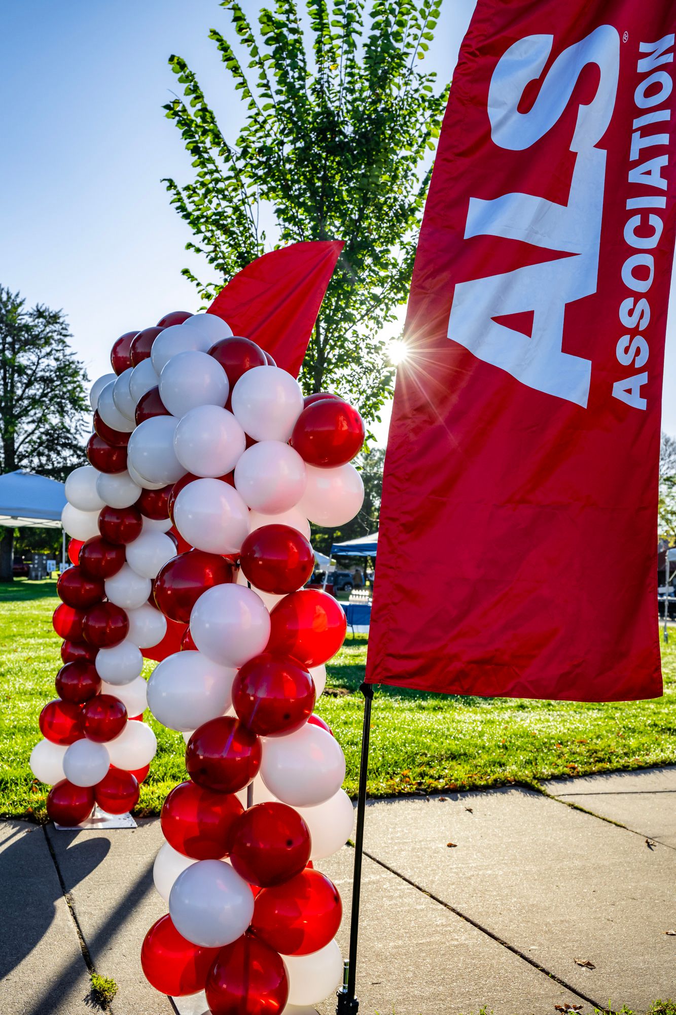 Red and white balloon arch decorations against blue sky at outdoor event.