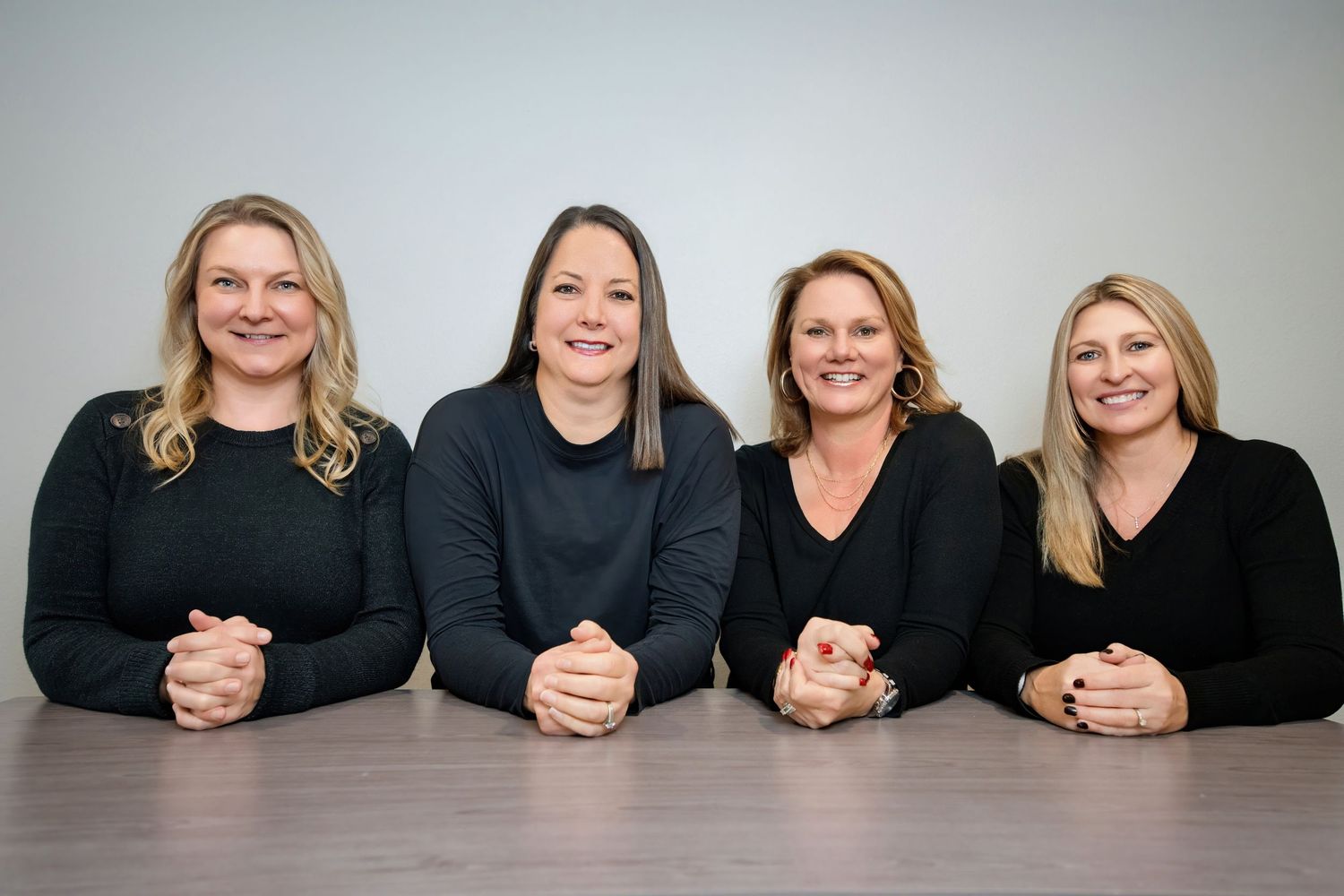 Four women wearing black tops seated at a table smiling at the camera.