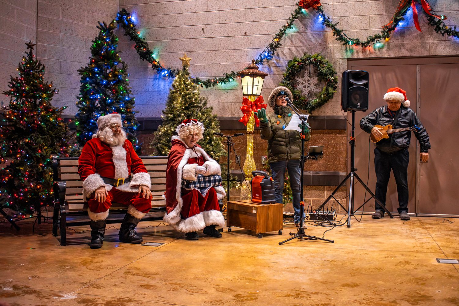 Holiday event setup with decorated Christmas trees and stage area in indoor venue.