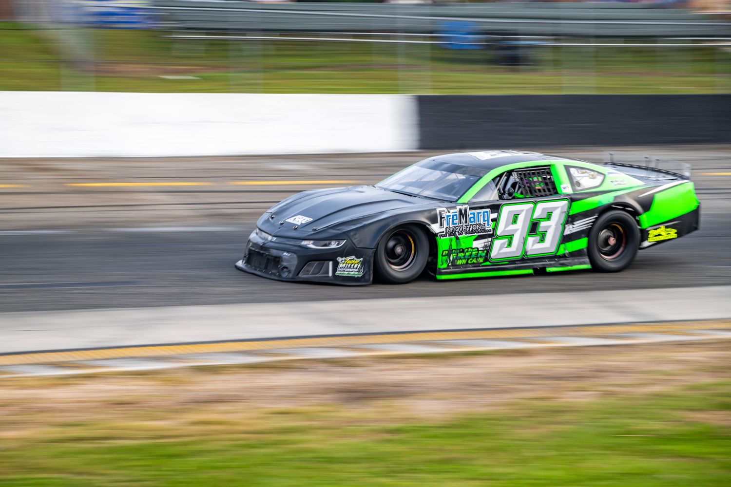 Green and black race car speeding around track during competitive motorsport event.