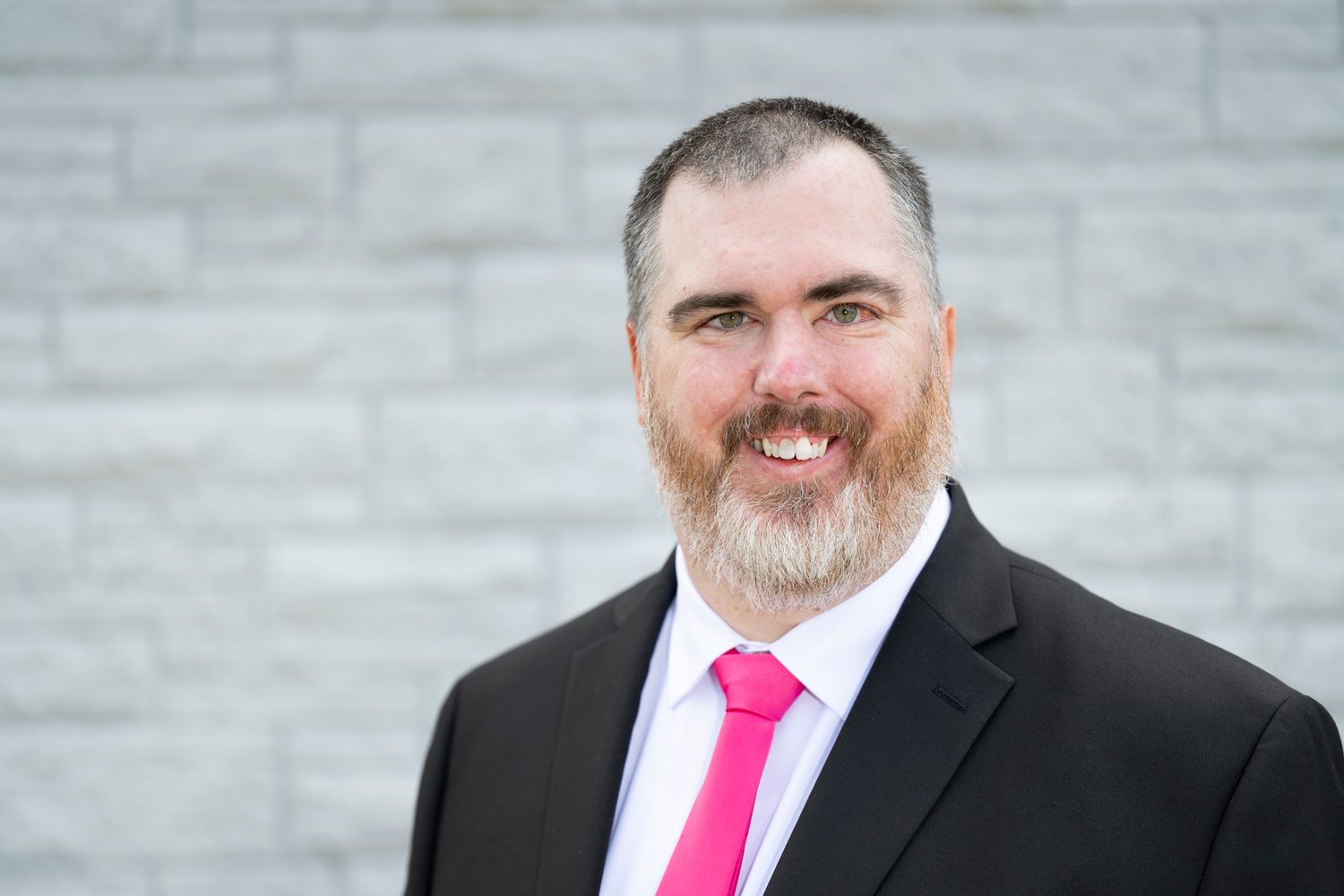 Professional portraits of a person in formal business attire with a pink tie against a grey background.