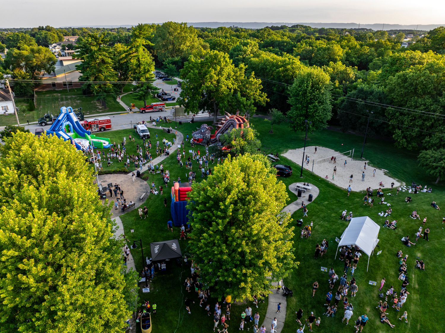 Aerial panoramic view of a community gathering with tents and activities in a park setting.