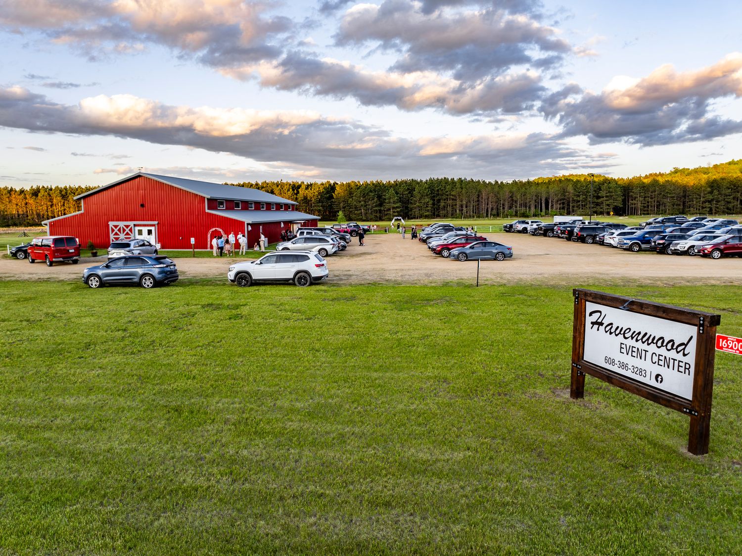 Large red barn venue with packed parking lot and event signage at sunset.