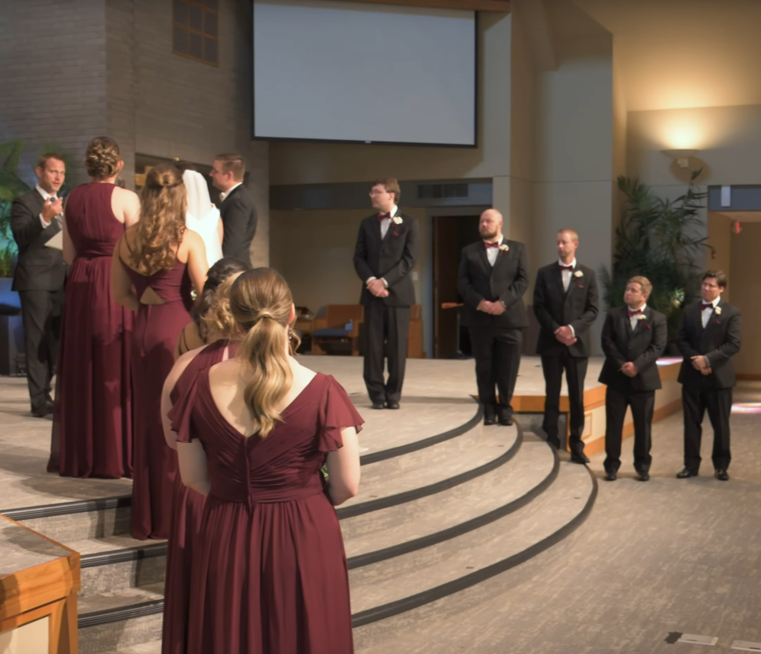 Wedding party lined up in burgundy dresses and dark suits for formal ceremony photos.