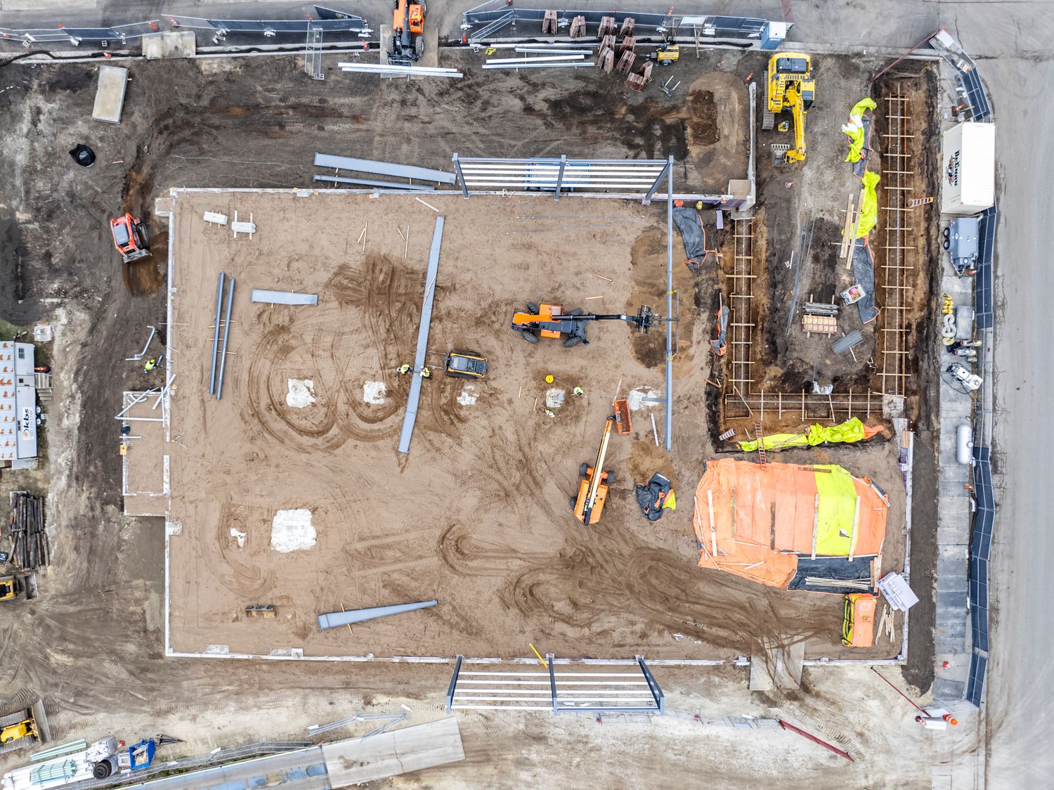 Construction site aerial view showing foundation work with pipes and equipment.