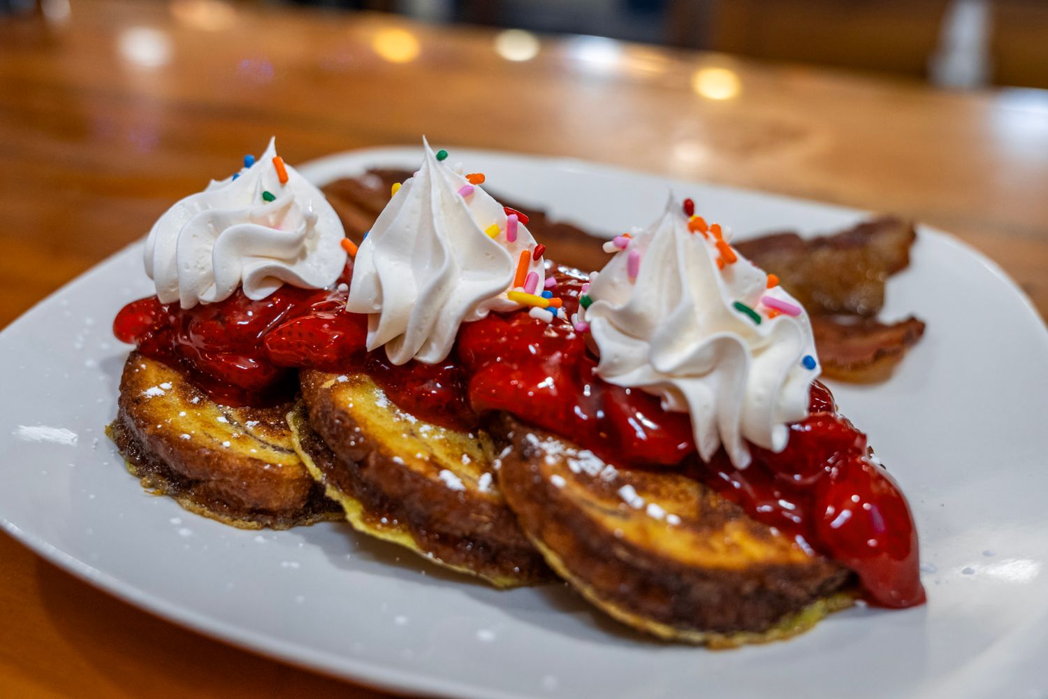 French toast topped with strawberry sauce and whipped cream dollops on a white plate.