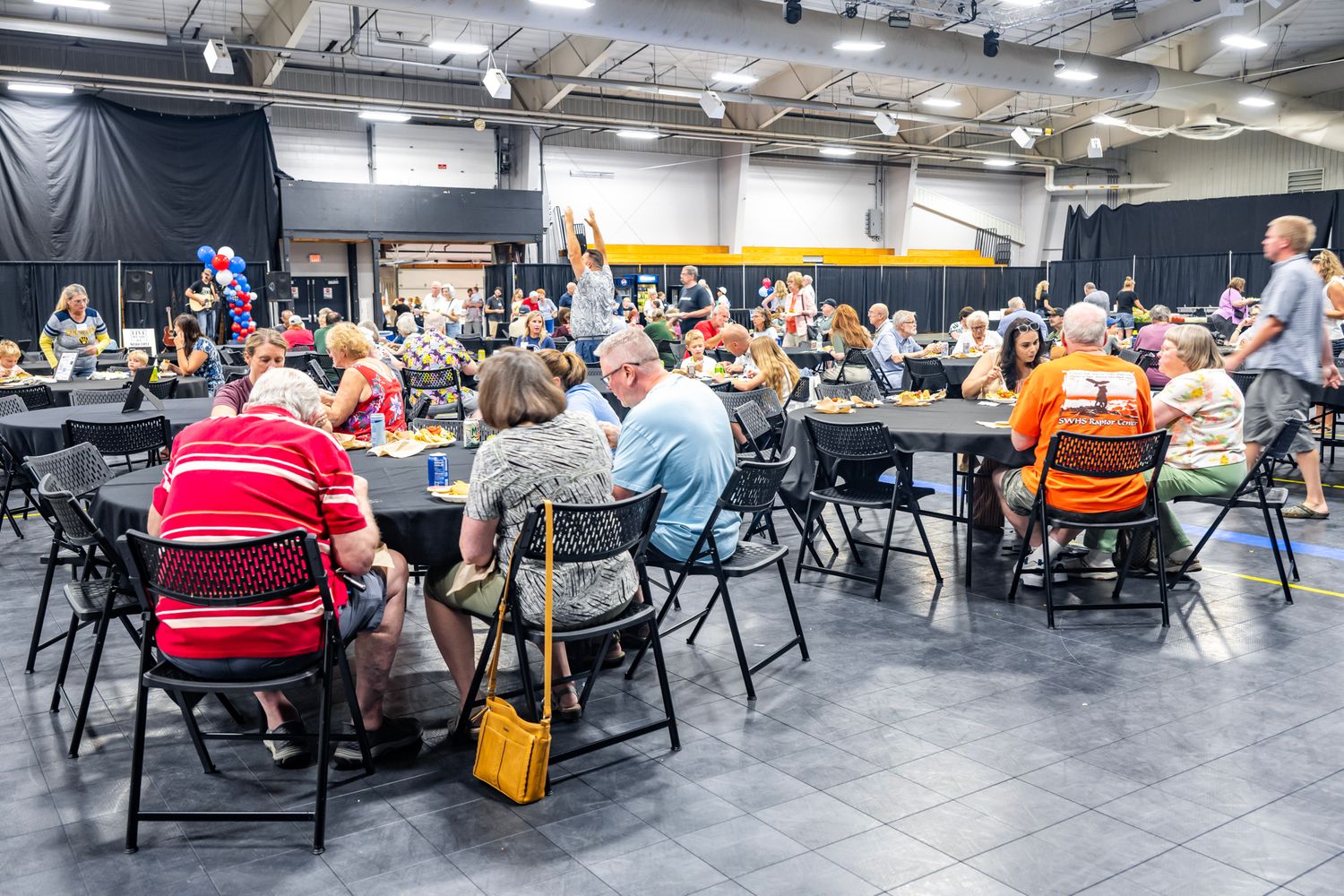 Wide view of a large indoor event space with multiple tables and attendees seated throughout.