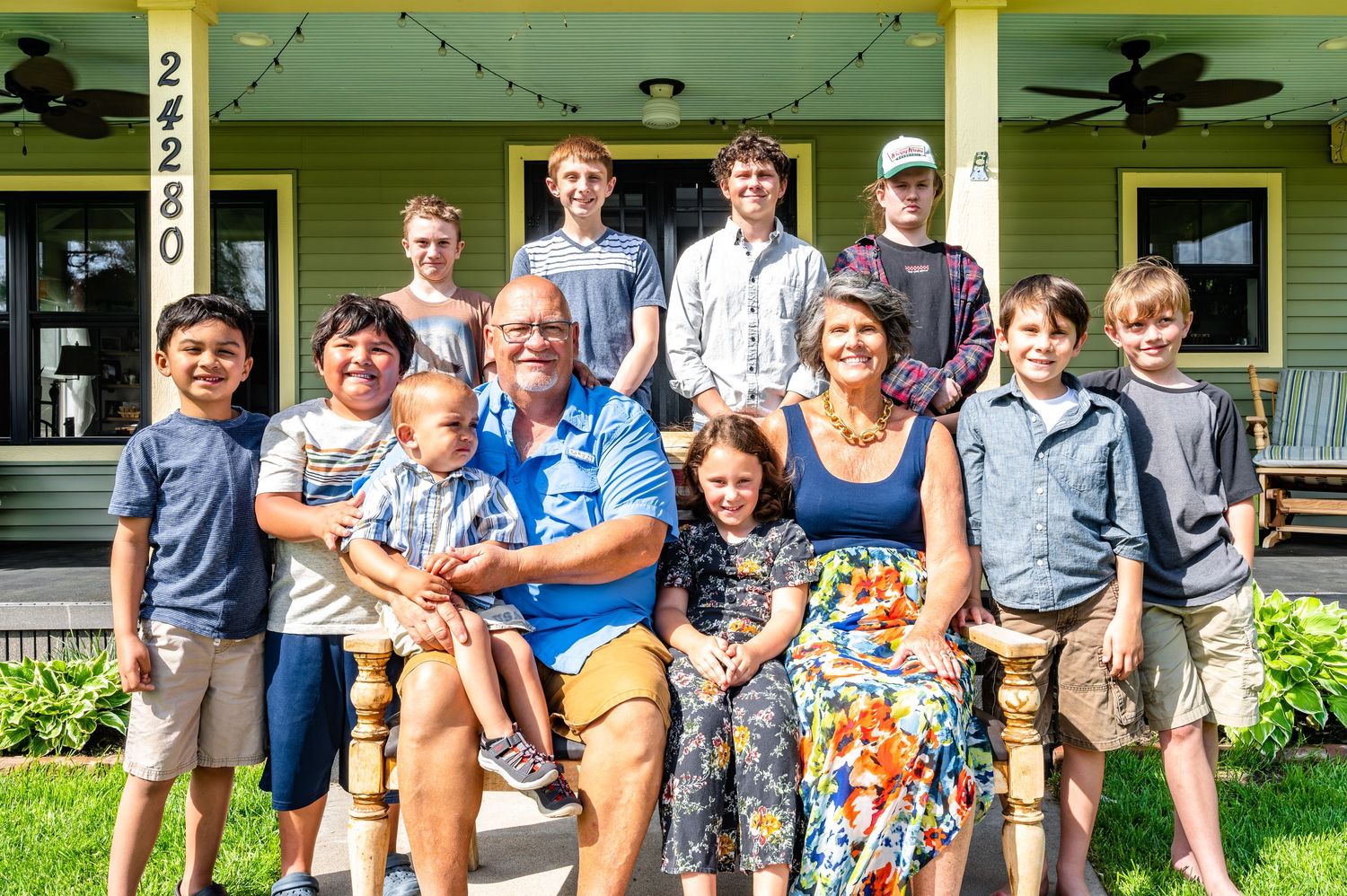 Large group photo of extended family gathered on green porch of country house.